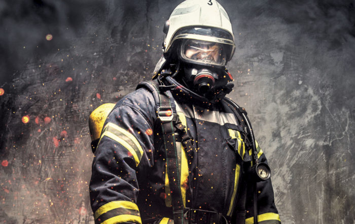 Ein Feuerwehrmann in voller Schutzausrüstung inklusive Atemschutzmaske, umgeben von Rauch und Funken