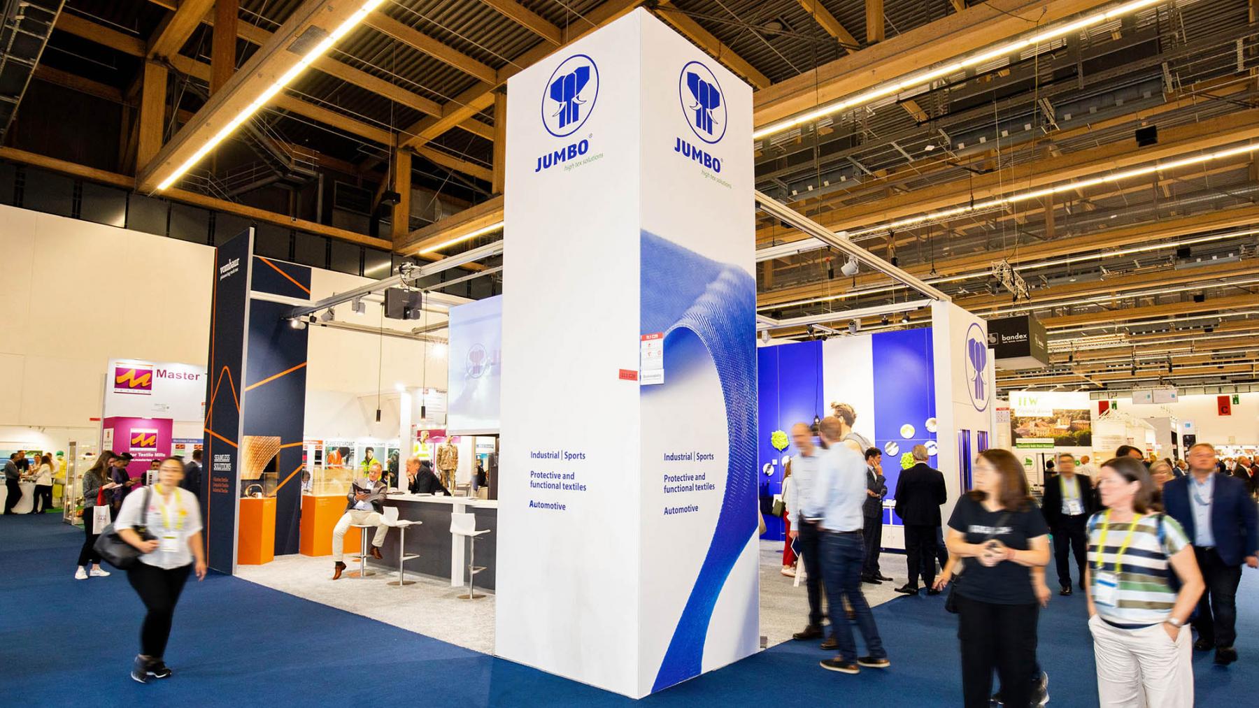JUMBO-Textil-Innovationen auf der techtextil 2022: Der blau-weiße Messestand von JUMBO-Textil als Vollansicht, Messebesucher in Bewegungsunschärfe auf dem Gang