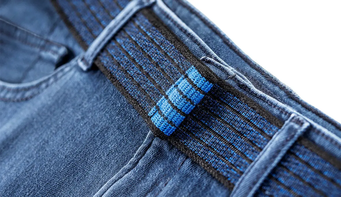 Nahaufnahme eines schwarz-blauen Klettgürtels, der durch Gürtelschlaufen einer Jeans geführt ist.