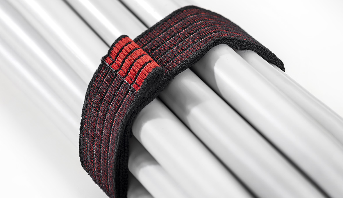 Elastikband klettfähig: Foto eines schwarz-roten Klettgürtels, der mehrere graue Rohre zusammenhält.